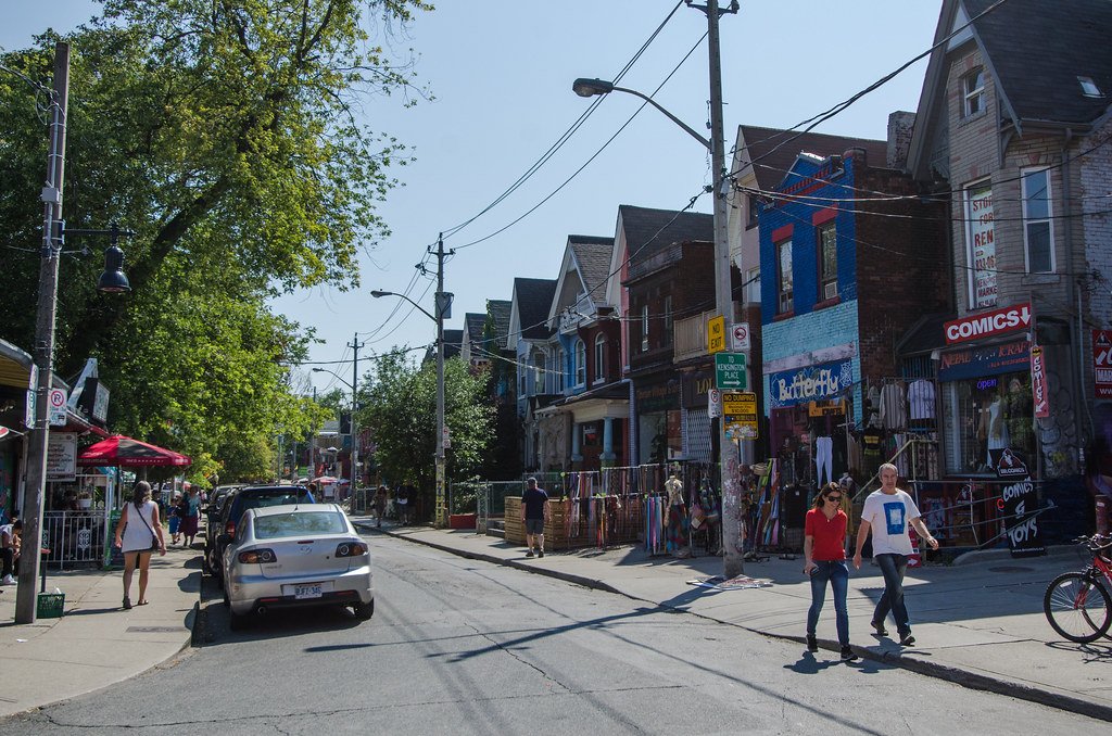 A lively and colorful street scene in Kensington Market, Toronto, showing pedestrians exploring vibrant shops and historic architecture