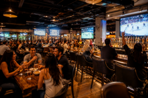 A vibrant interior view of a modern sports bar filled with fans watching a game on massive screens while enjoying refreshments.